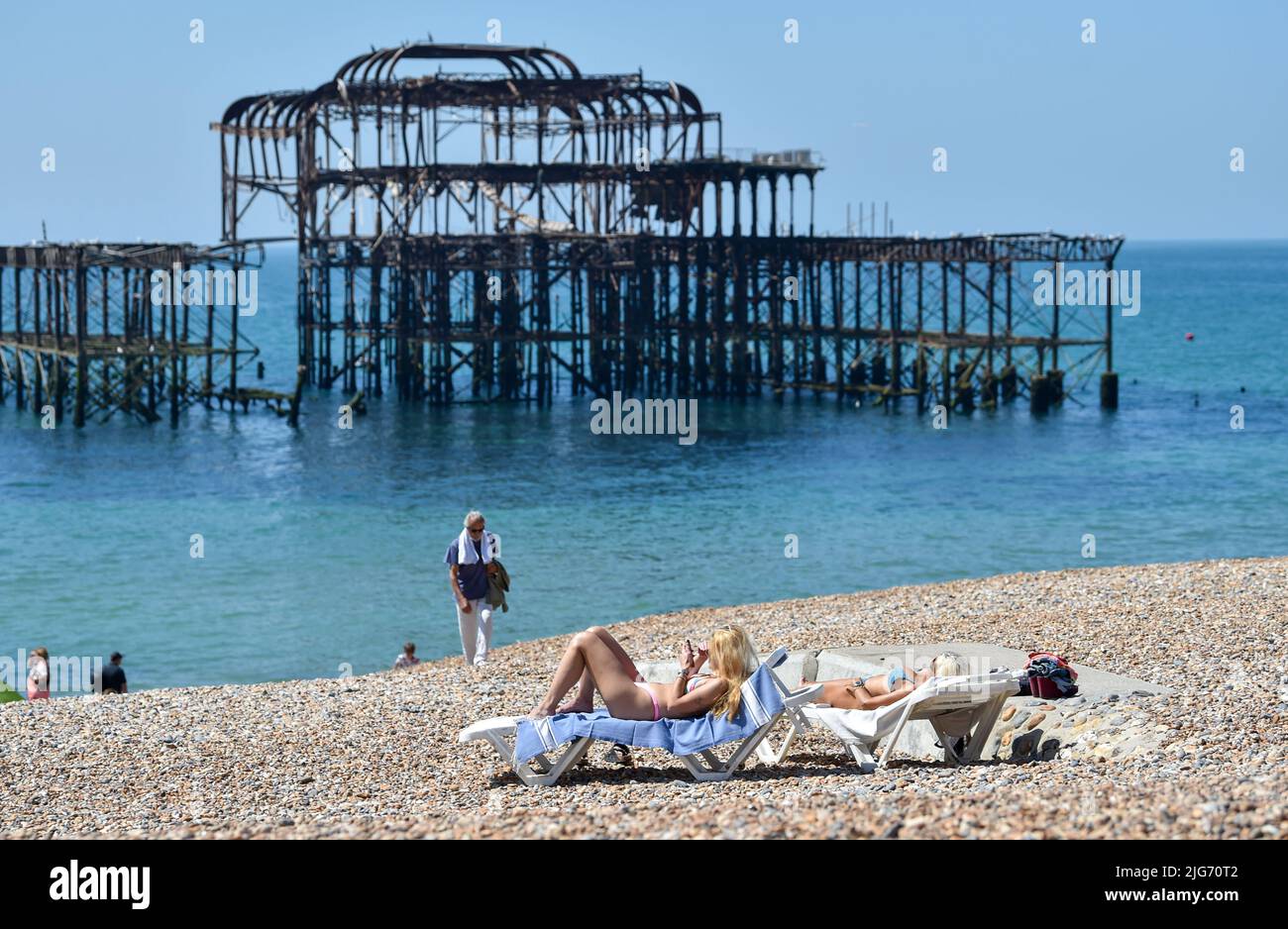 Brighton UK 8th July 2022 - Sunbathers enjoy the beautiful hot sunshine on Brighton beach  by the West Pier as a possible heatwave is forecast for parts of the UK over the next week .  : Credit Simon Dack / Alamy Live News Stock Photo