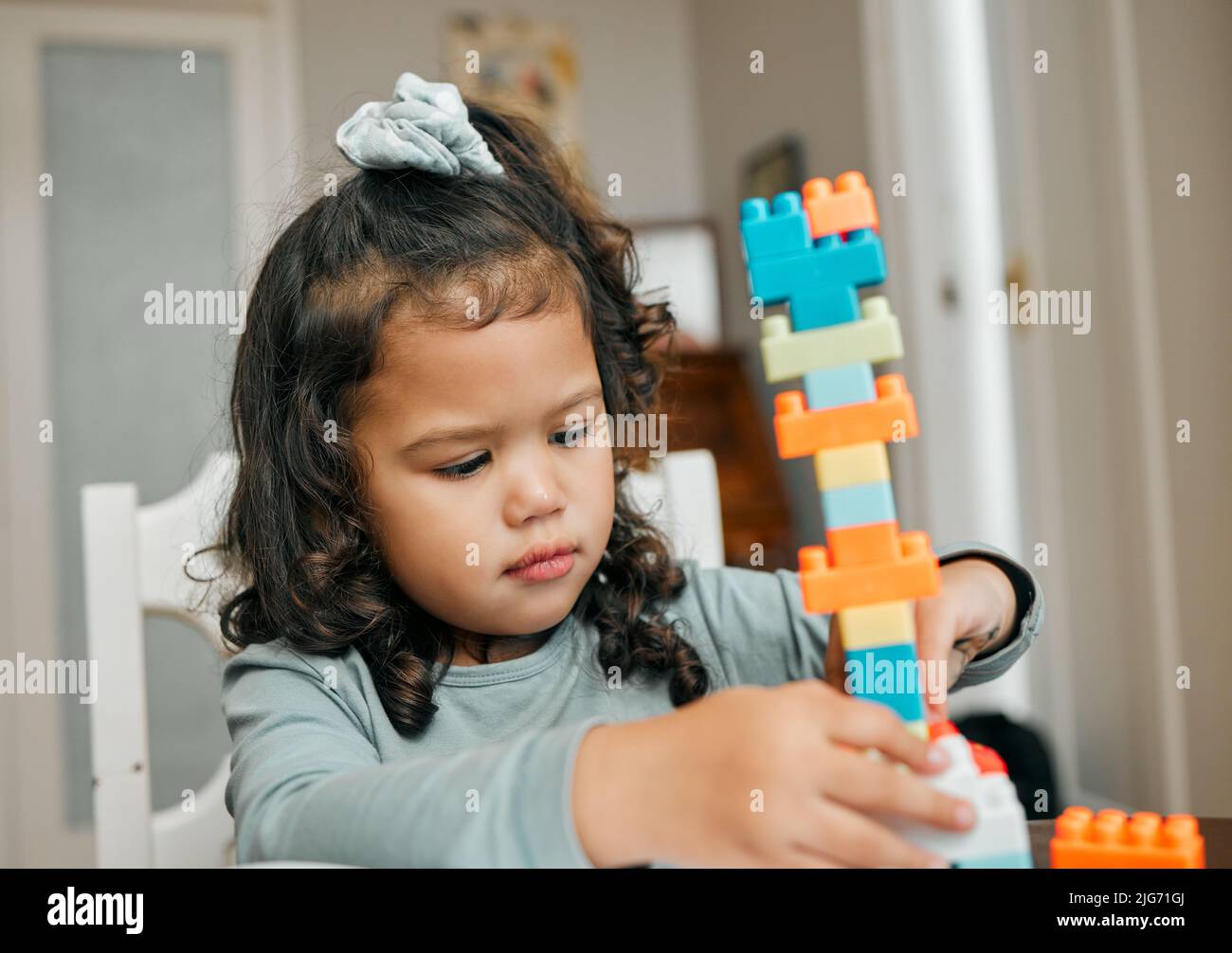 Really goos for hand and eye coordination. Shot of a cute little girl playing with building blocks at the kitchen table. Stock Photo