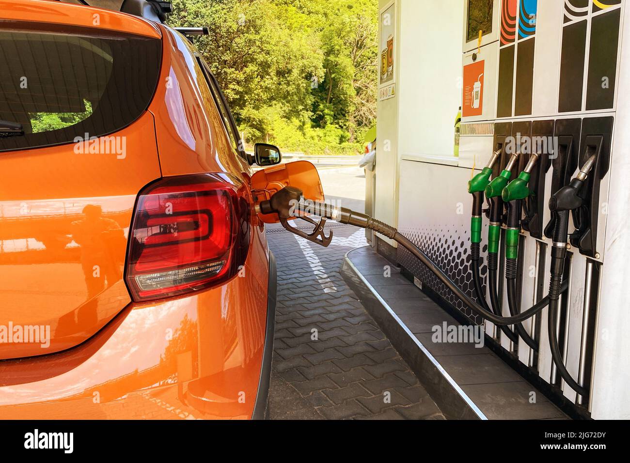 Fill car with fuel in petrol station. Pumping gasoline fuel in orange car at a gas station in city. Stock Photo