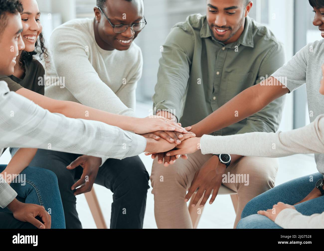 We can overcome this together. Shot of a diverse group of people sitting together and stacking their hands in the middle. Stock Photo