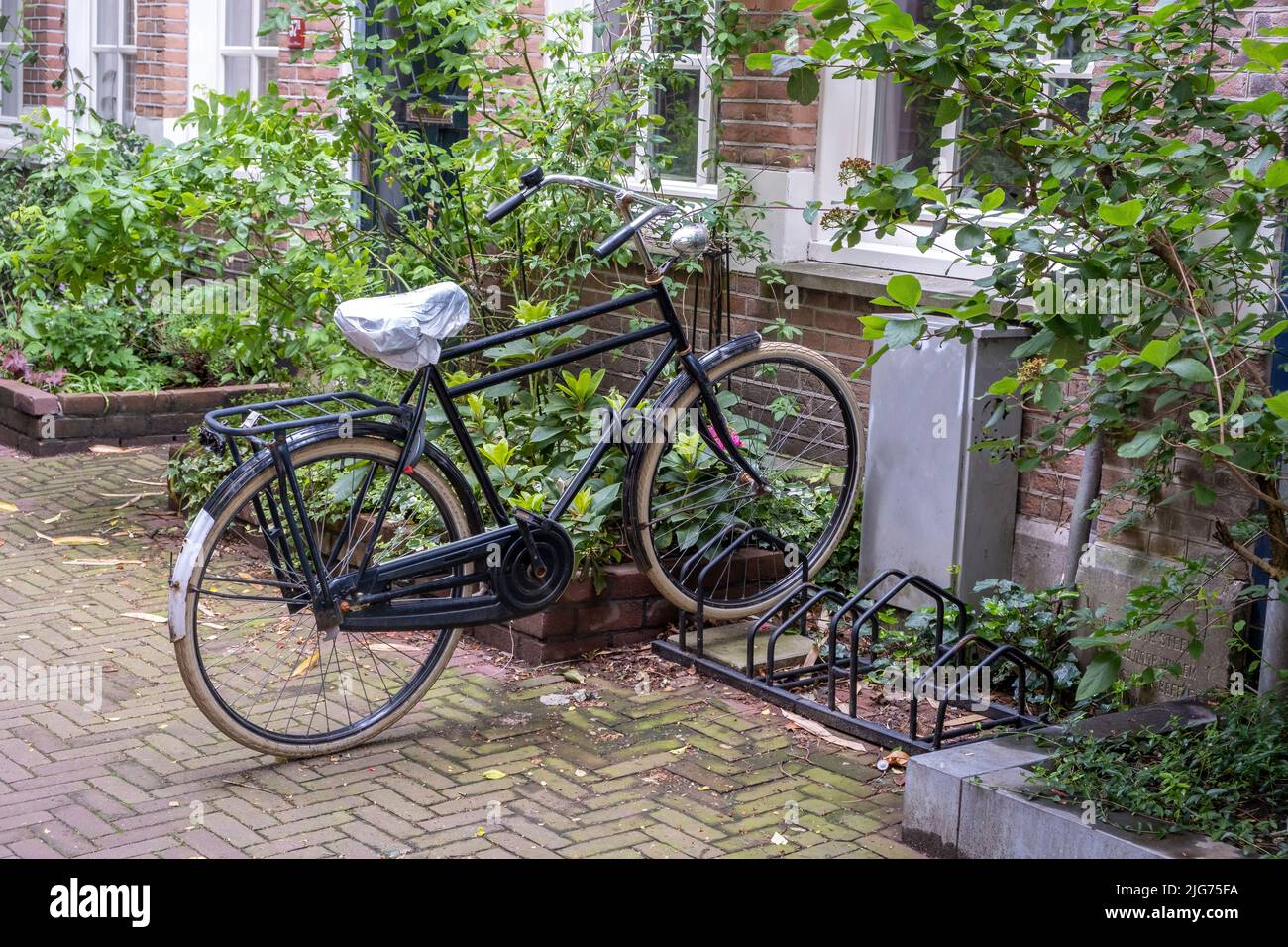 Βιcycle parked in front of a building, Amsterdam city neighborhood. Traditional red brick wall house, paved alley. Holland Netherlands Stock Photo