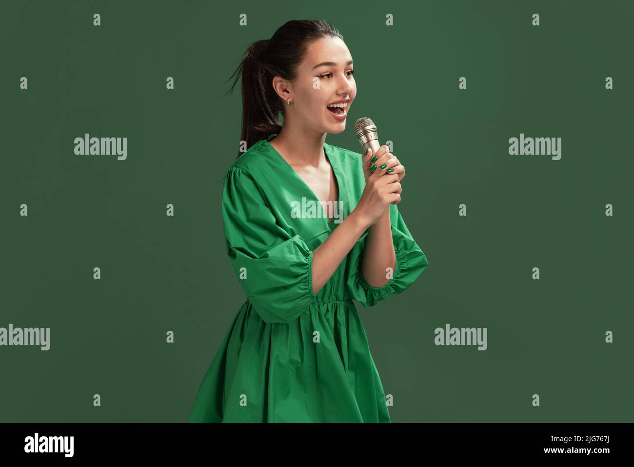 Portrait of beautiful young girl posing in dress, singing in microphone ...