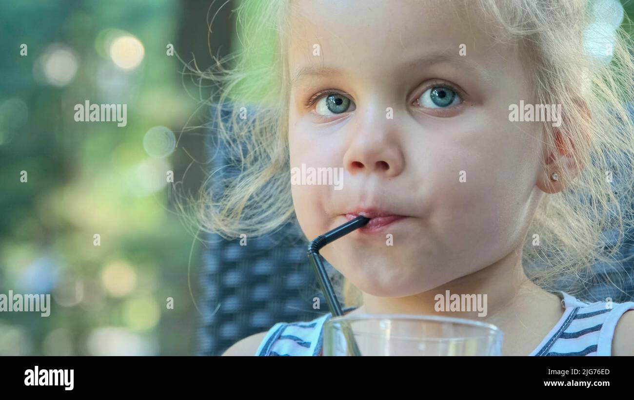 Cute little girl drinks juice through straw. Closeup portrait of
