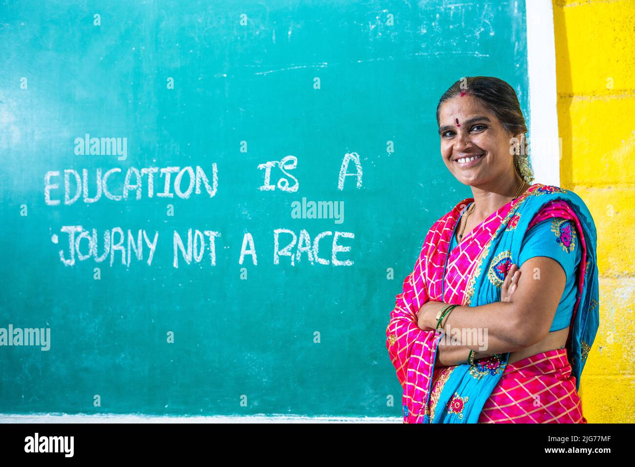 Portrait shot of happy smiling teacher with crossed arms standing in front of chalk board at classroom by looking at camera - concept of professional Stock Photo
