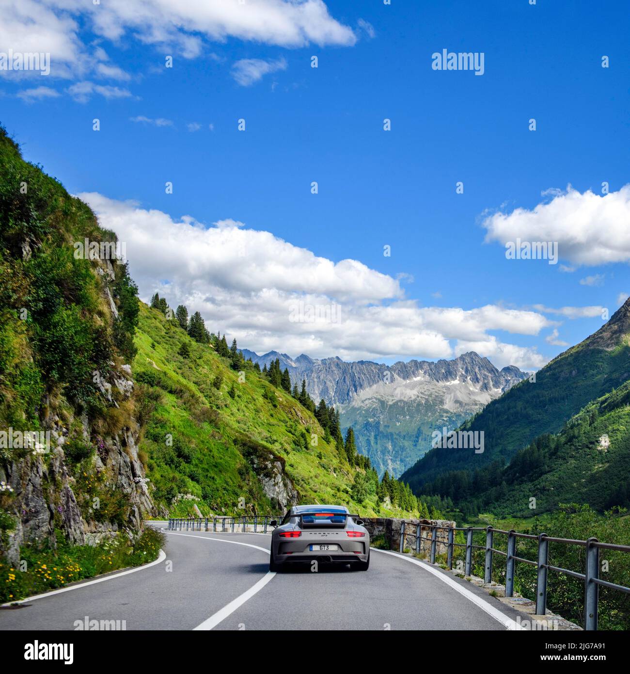Supercar sports car GT3 driving on road from Sustenpass to Wassen, in the background mountain range with peaks without snow above tree line, Canton Stock Photo