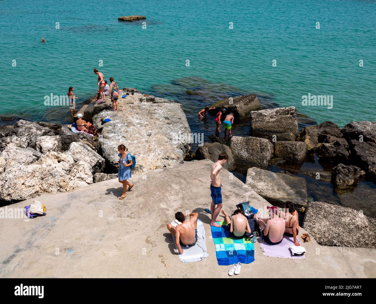 Diverse groups of people enjoying a swim and sunbathing on the rocks of the bay of Otranto on a hot summer day Stock Photo