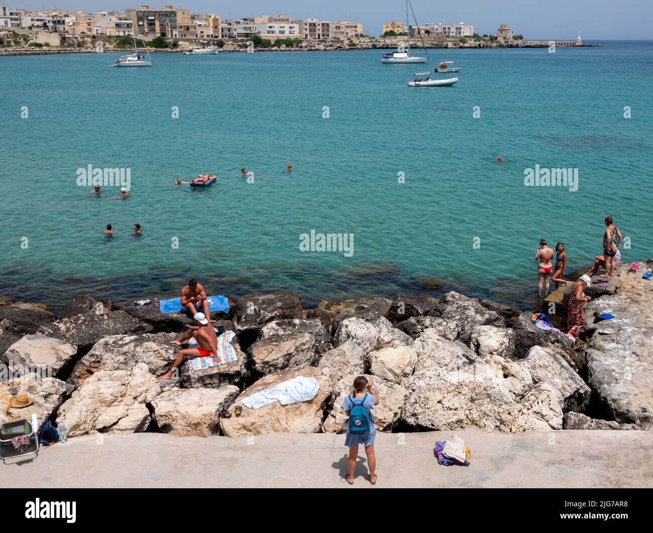Diverse groups of people enjoying a swim and sunbathing on the rocks of the bay of Otranto on a hot summer day Stock Photo