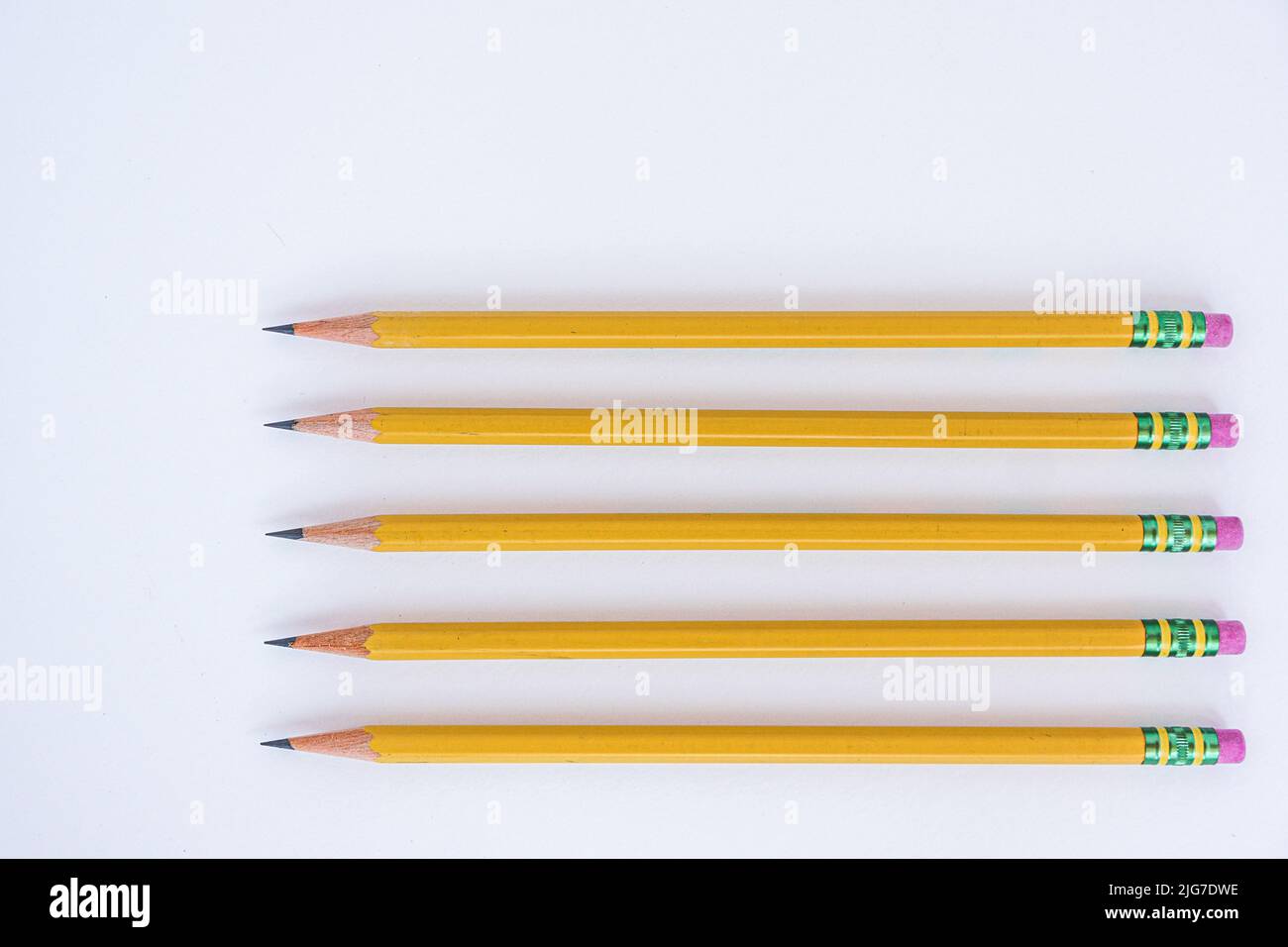 Negative space is utilized with five sharp pencils lined up on a white sheet of paper pointing to the left. Stock Photo