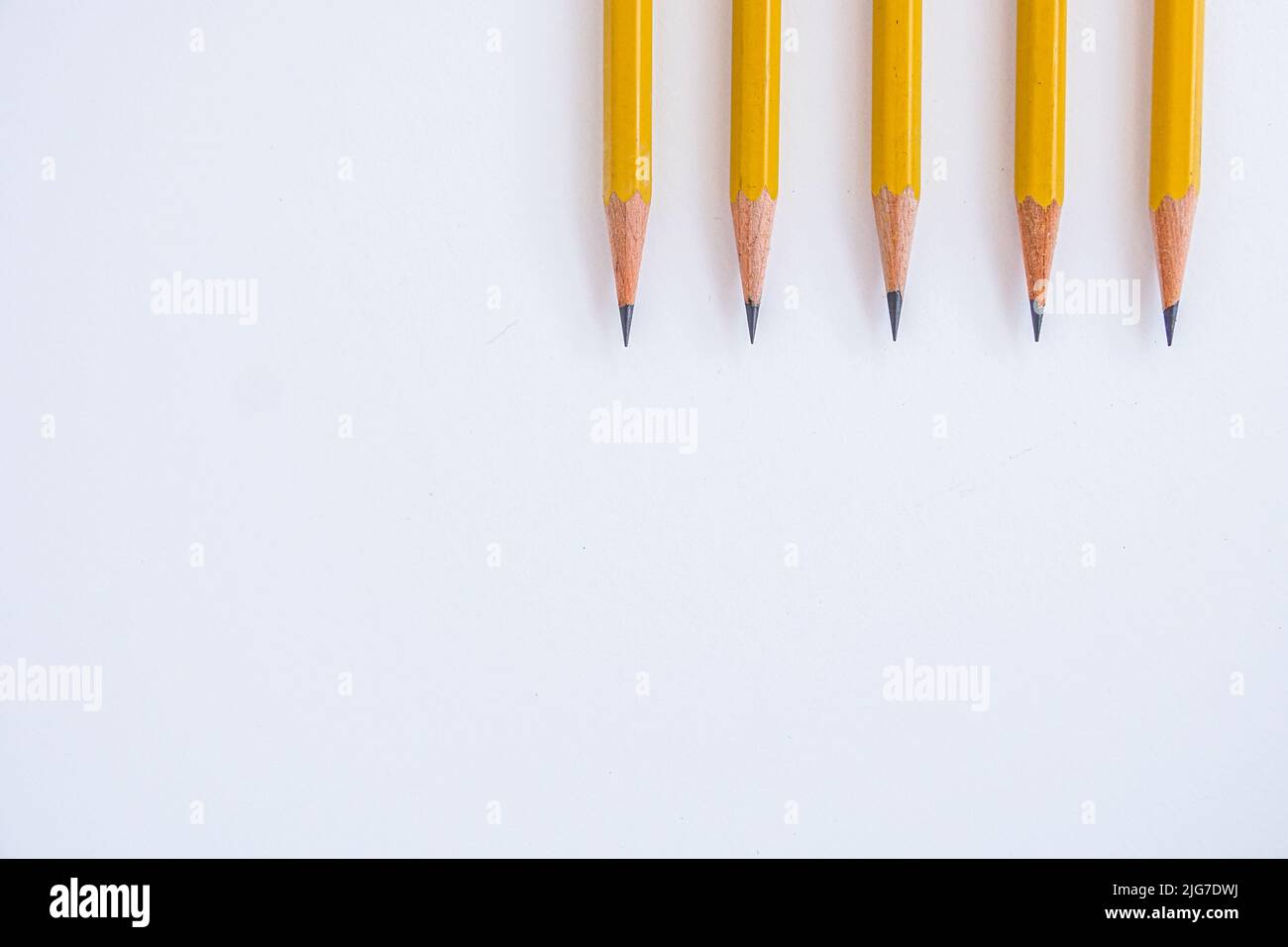 Negative space is utilized with five sharp pencils lined up on a white sheet of paper pointing downward. Stock Photo