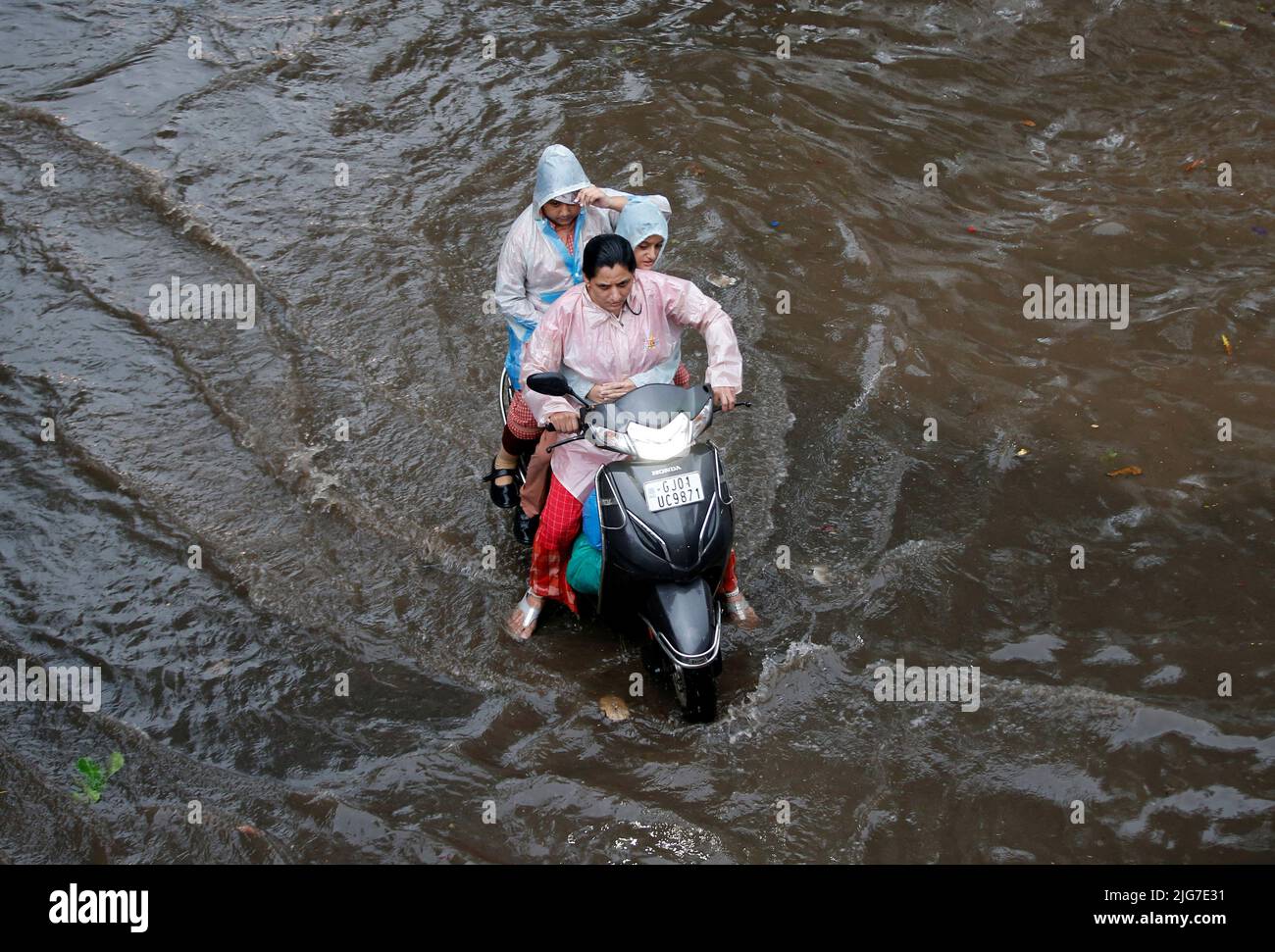 A woman with her children, balances her scooter as she moves through a water-logged road after heavy rains in Ahmedabad, India, July 8, 2022. REUTERS/Amit Dave Stock Photo