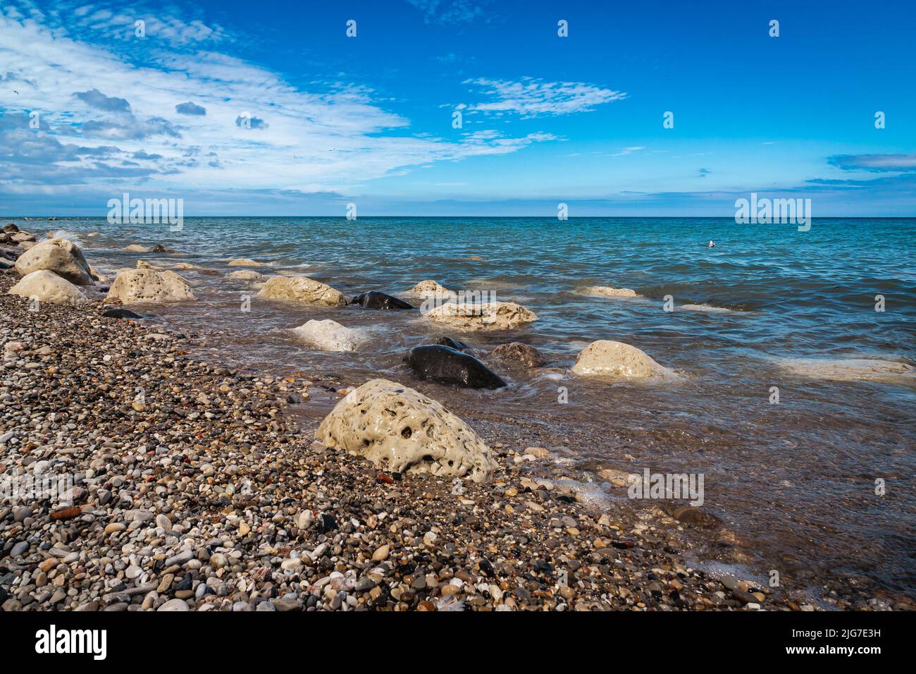 Different colored boulders sit in the water along the rocky shoreline of Lake Michigan under a blue cloudy sky in Wisconsin. Stock Photo