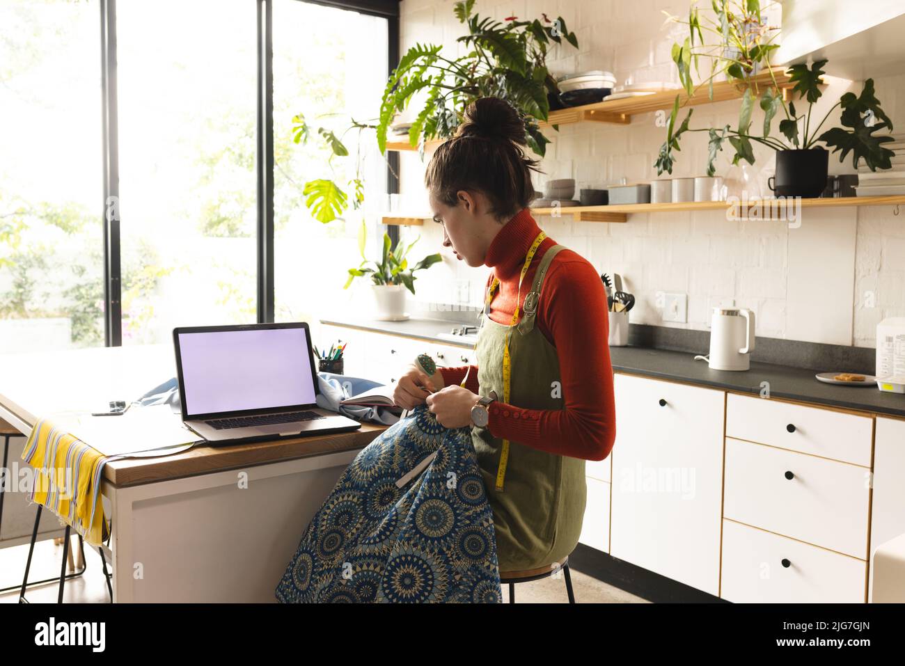 Image of caucasian non-binary trans woman with laptop working in sewing workshop Stock Photo