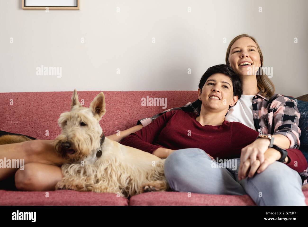 Caucasian woman lying on happy girlfriend's shoulder while relaxing with scottish terrier on sofa Stock Photo