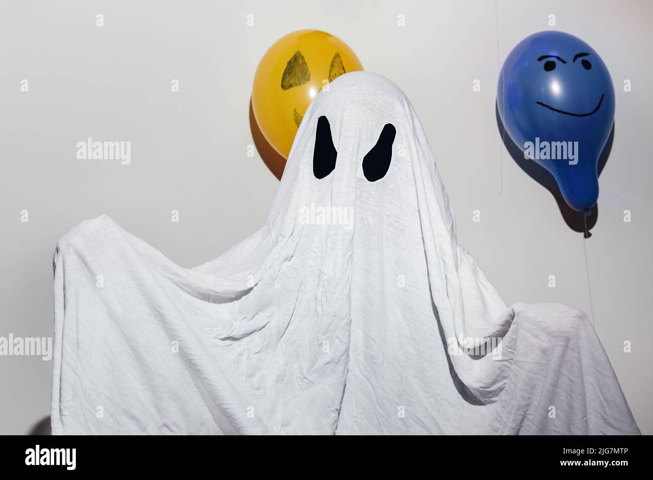 Happy Halloween. A child in a white homemade ghost costume and painted orange and blue balls. Paper eyes. Festive design, party concept. All Saints' Day celebration. Stock Photo