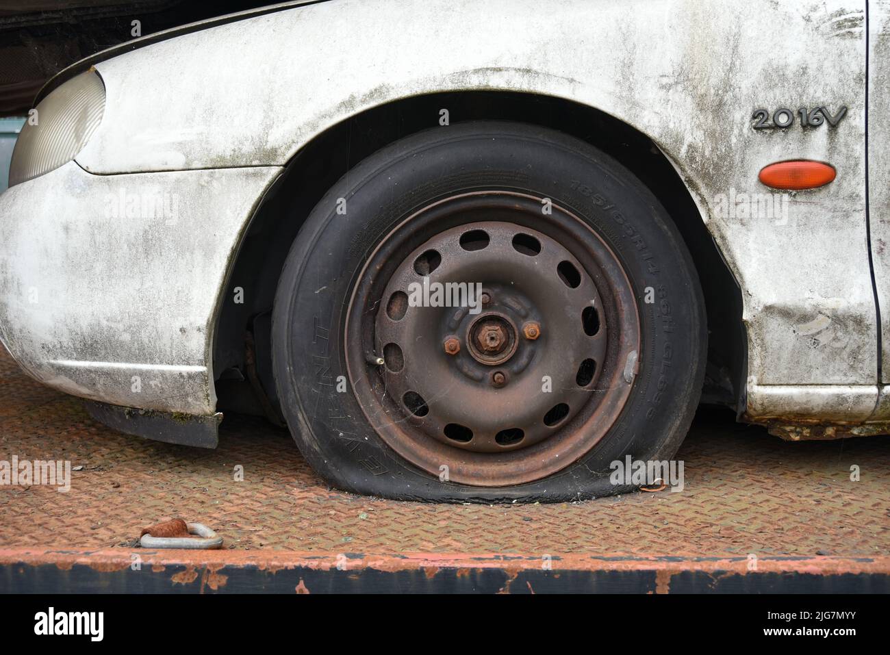 Dirty old car with a flat tyre loaded on to a truck heading for the scrap yard. Stock Photo