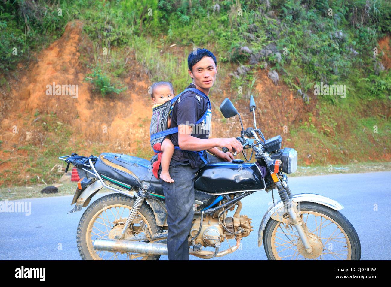 Ethnic minority man riding a motorbike on the road with his child Stock Photo
