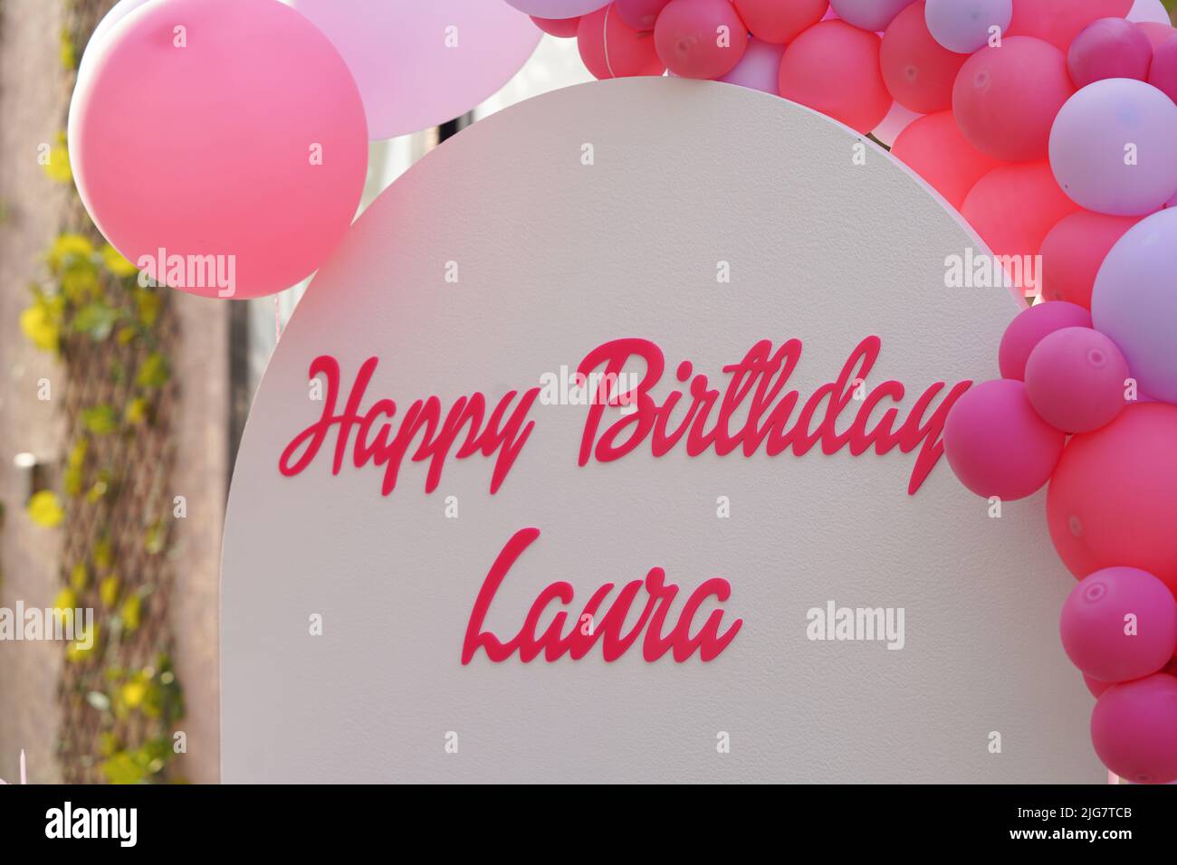 Happy birthday Laura banner, background with pink and purple balloons and some grass on the wall. Stock Photo