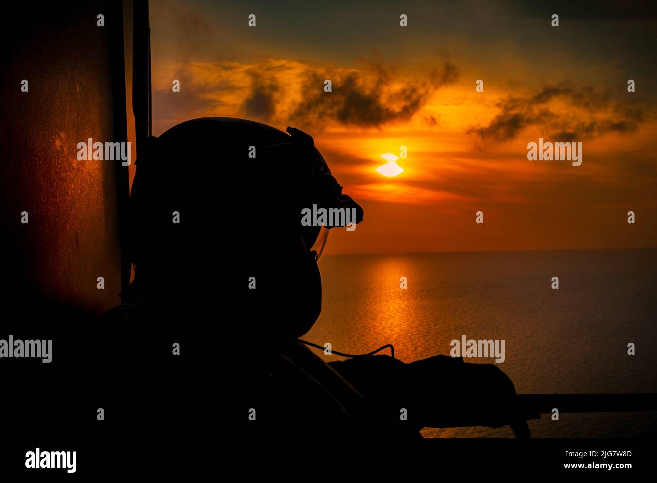 The silhouette of flight engineer of helicopter flying at sunset in the Bahamas Stock Photo