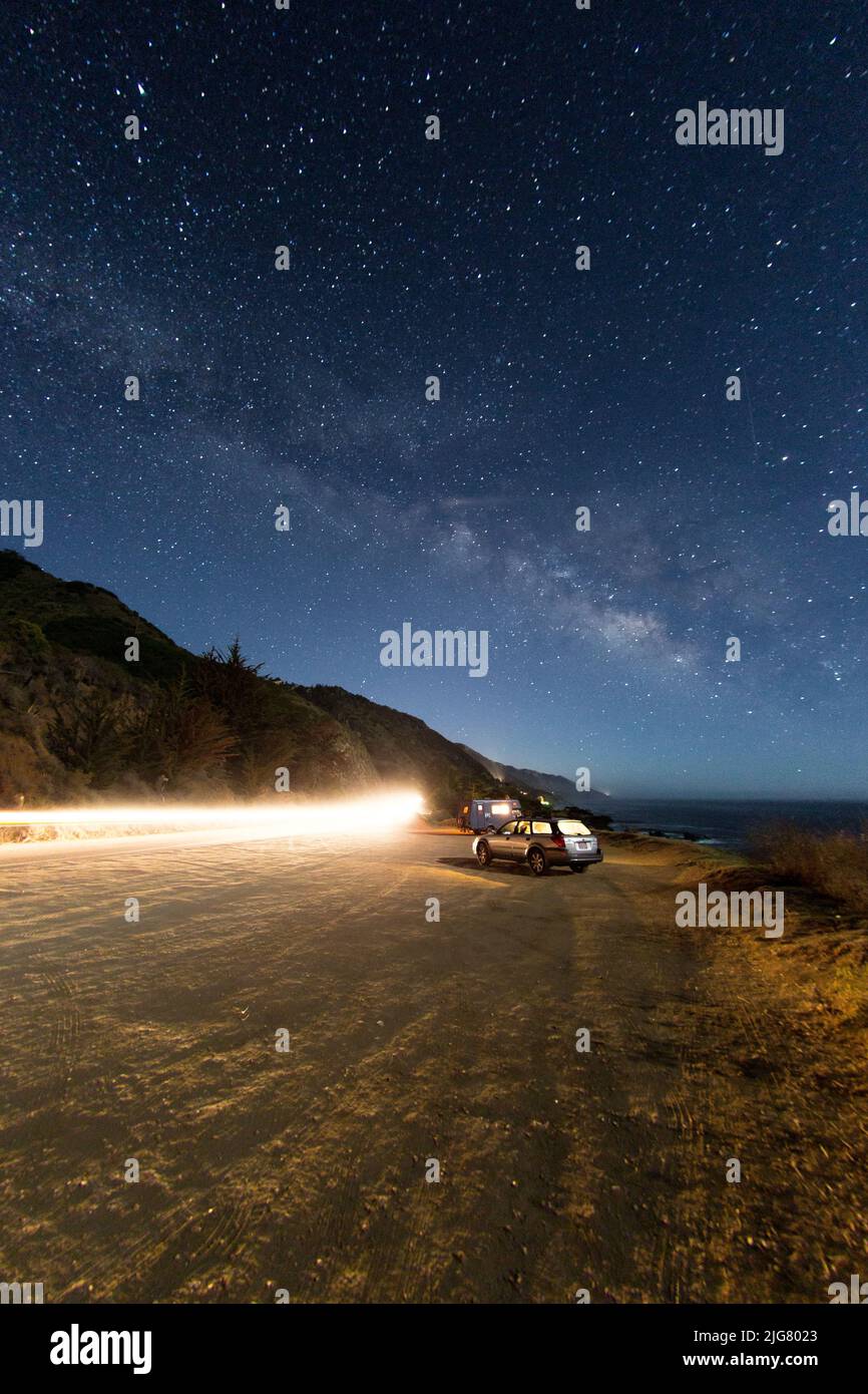 A vertical shot of cars and lights on a dirt road under the starry sky ...