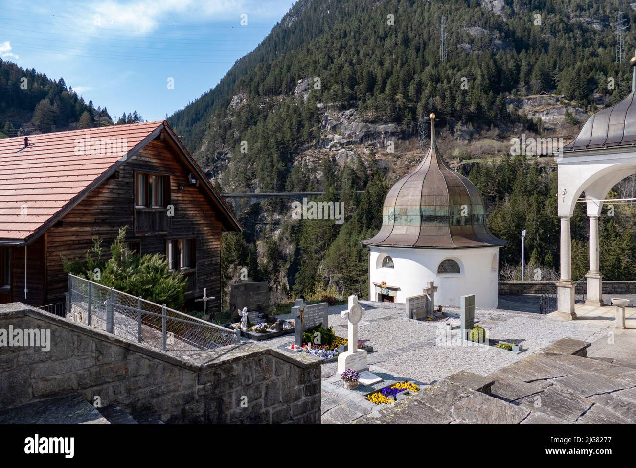 A circular cemetery chapel in front of Wassen church with tombs surrounded by mountains in Switzerland Stock Photo