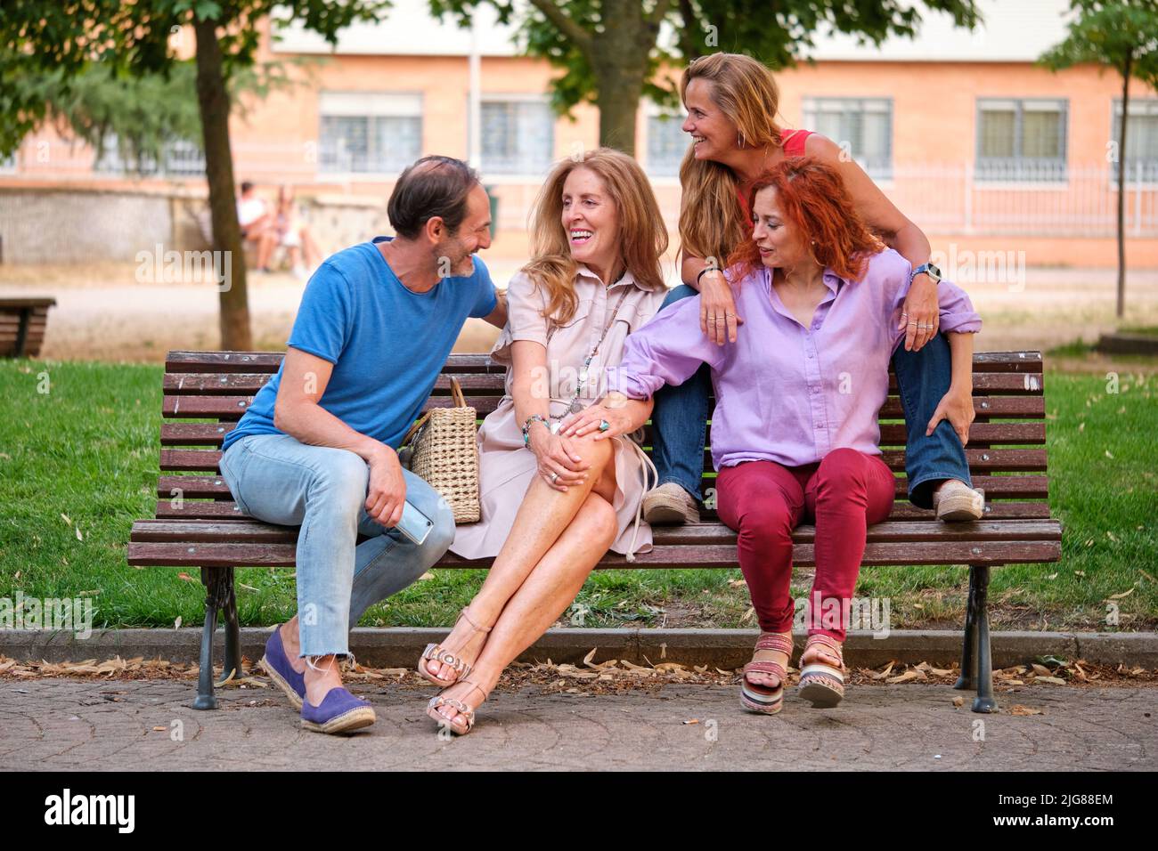 Four mature adults talking and laughing sitting on a bench in a park. Stock Photo