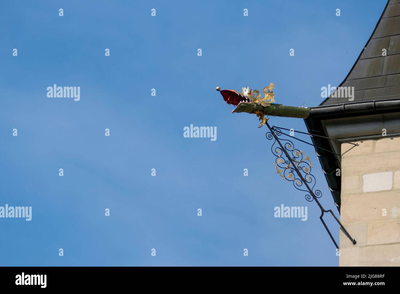 A metal dragon gutter spout looking over the edge of a roof on blue sky