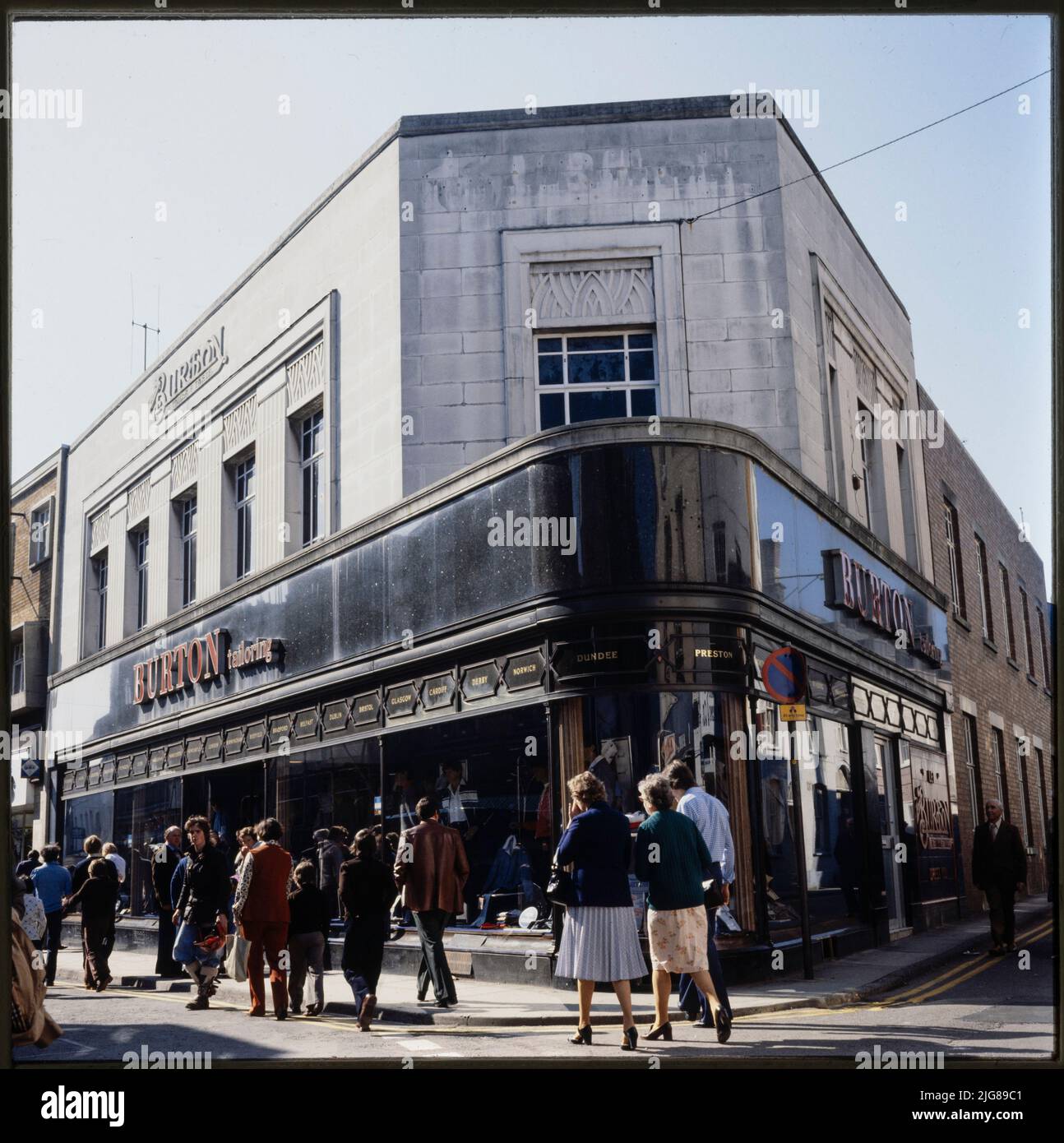 Burton, 16-18 High Street, Abergavenny, Monmouthshire, Wales, 1980s-1990s. The Burton store at 16-18 High Street, showing the carved logo, polished dark stone facade, and chain of merit transom lights. The Burton store in Abergavenny was built in 1937, and a foundation stone was laid by Raymond Montague Burton in that year. The store was designed by their in-house architect Nathaniel Martin. It features common Burton motifs including the logo carved in relief in stone, the 'chain of merit' transom lights at the top of the shopfront windows, and the fascia of polished dark stone. Stock Photo