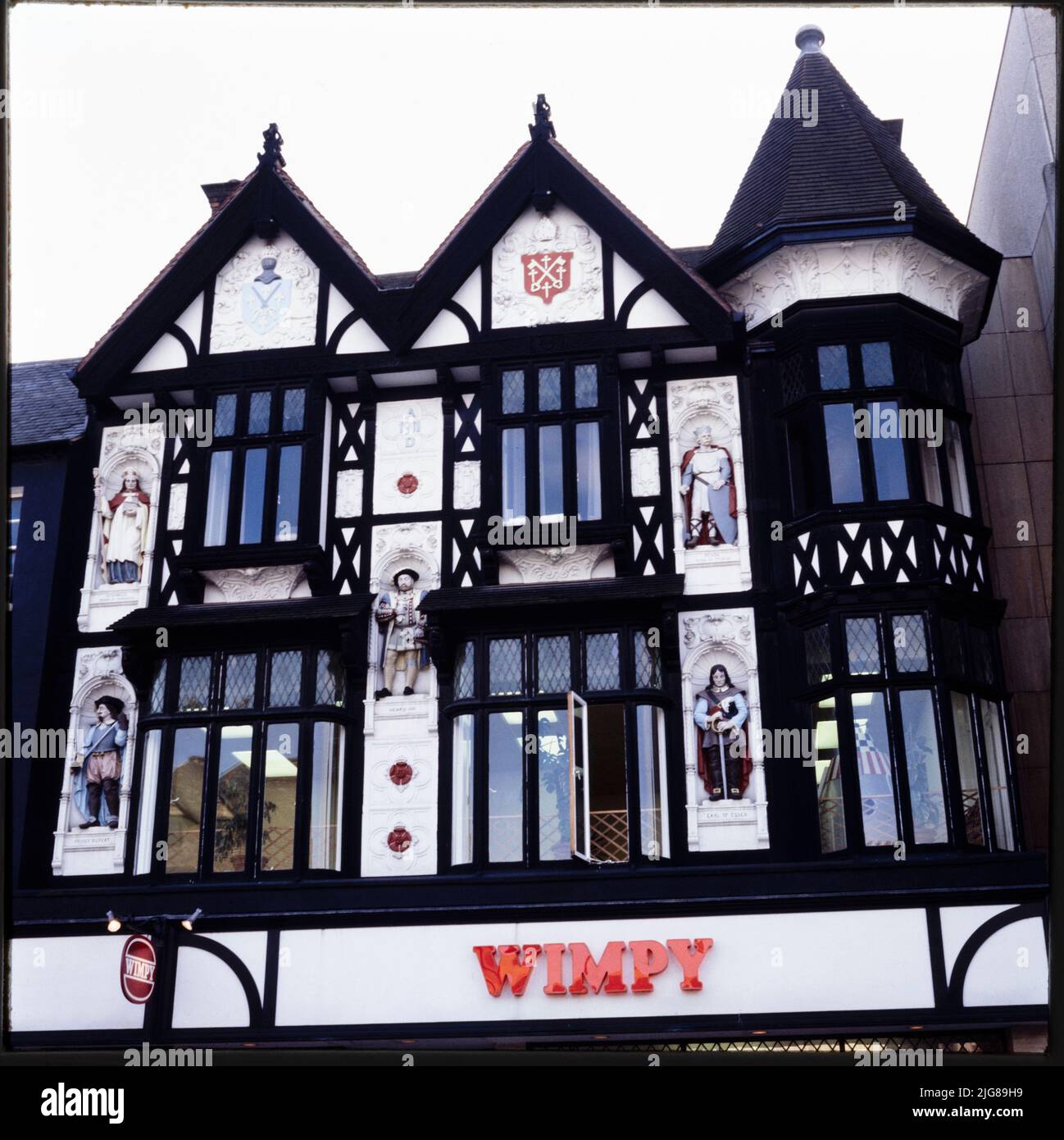 Cathedral Square, Peterborough, City of Peterborough, 1970s-1990s. The half-timbered upper elevation of 8 Cathedral Square, built as a Boots store, with painted statues in niches flanking the upper floor windows. The Boots store in Cathedral Square was is dated 1911, and was designed by Boots' in-house architect Michael Vyne Treleaven. The statues on the facade were sculpted by Gilbert Seale &amp; Son of Camberwell, London, and depict Athelwold, King Peada of Mercia, Henry VIII, Prince Rupert and the Earl of Essex. The premises were later occupied by Wimpy and Burger King restaurants. Stock Photo