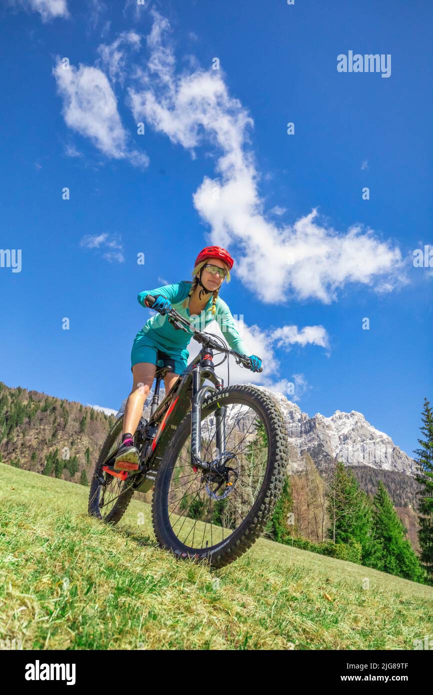 Caucasian blonde woman with sports technical clothing riding an e-bike in the mountains, dolomites, Belluno, Veneto, Italy Stock Photo