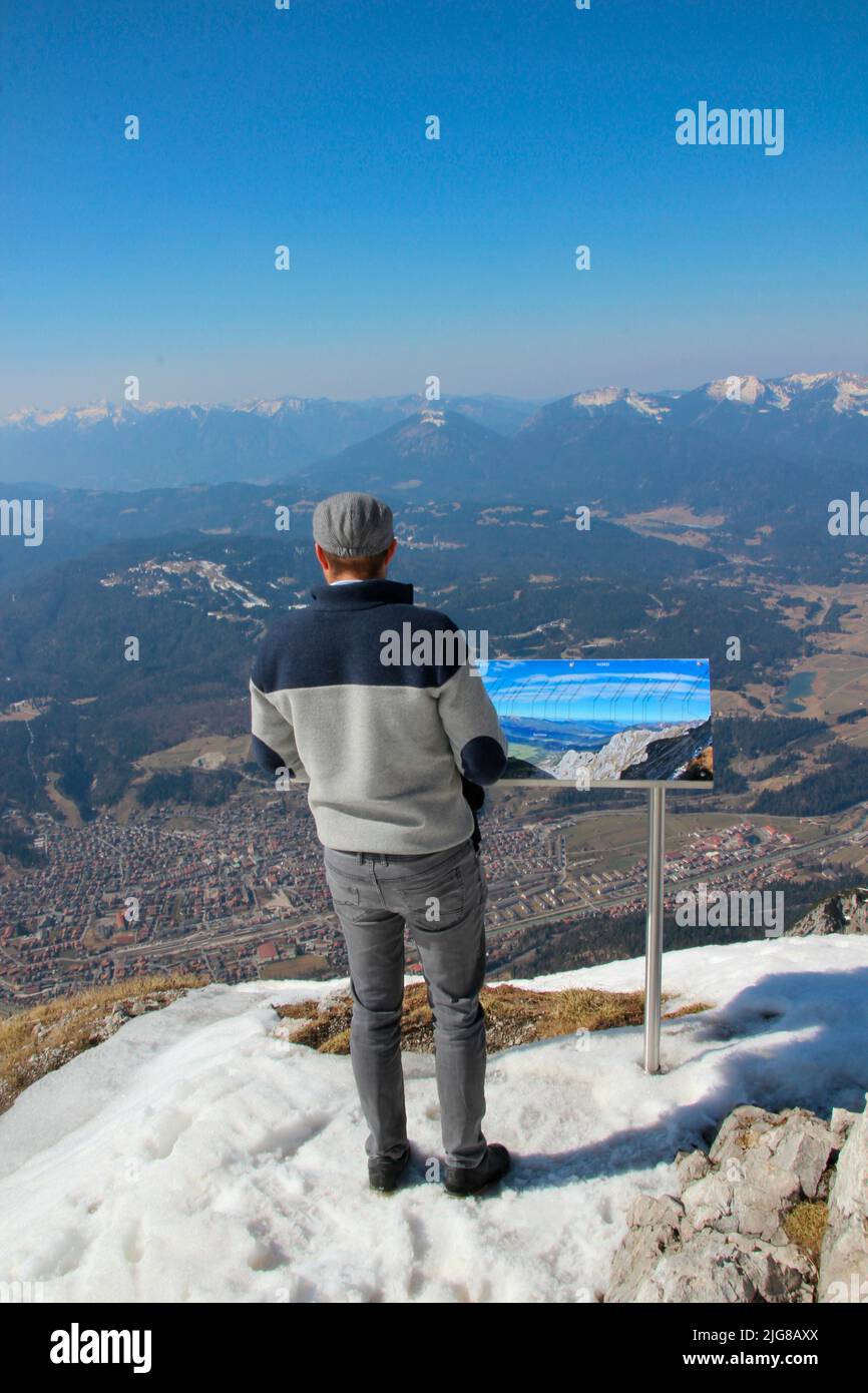 Young man, panoramic map, view from Karwendel, at the mountain station Karwendelbahn on the Estergebirge, in the foreground Mittenwald, against blue sky, Stock Photo