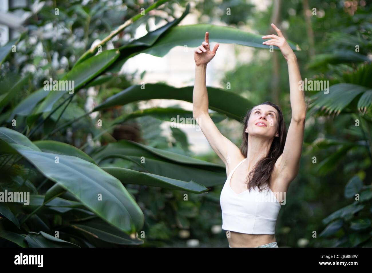 Female meditating and practicing yoga in tropical rainforest. Beautiful young woman practicing yoga outdoor with tropical forest in background. Stock Photo