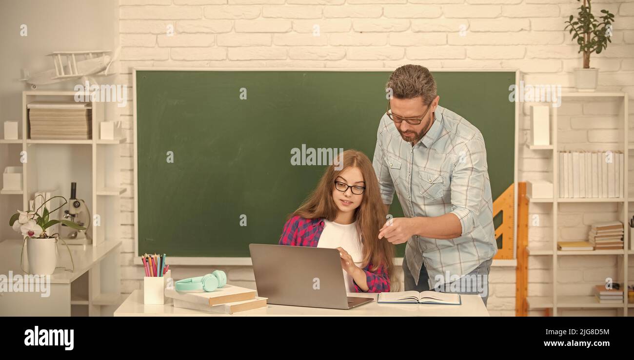 serious teen girl and teacher man in high school with pc at blackboard