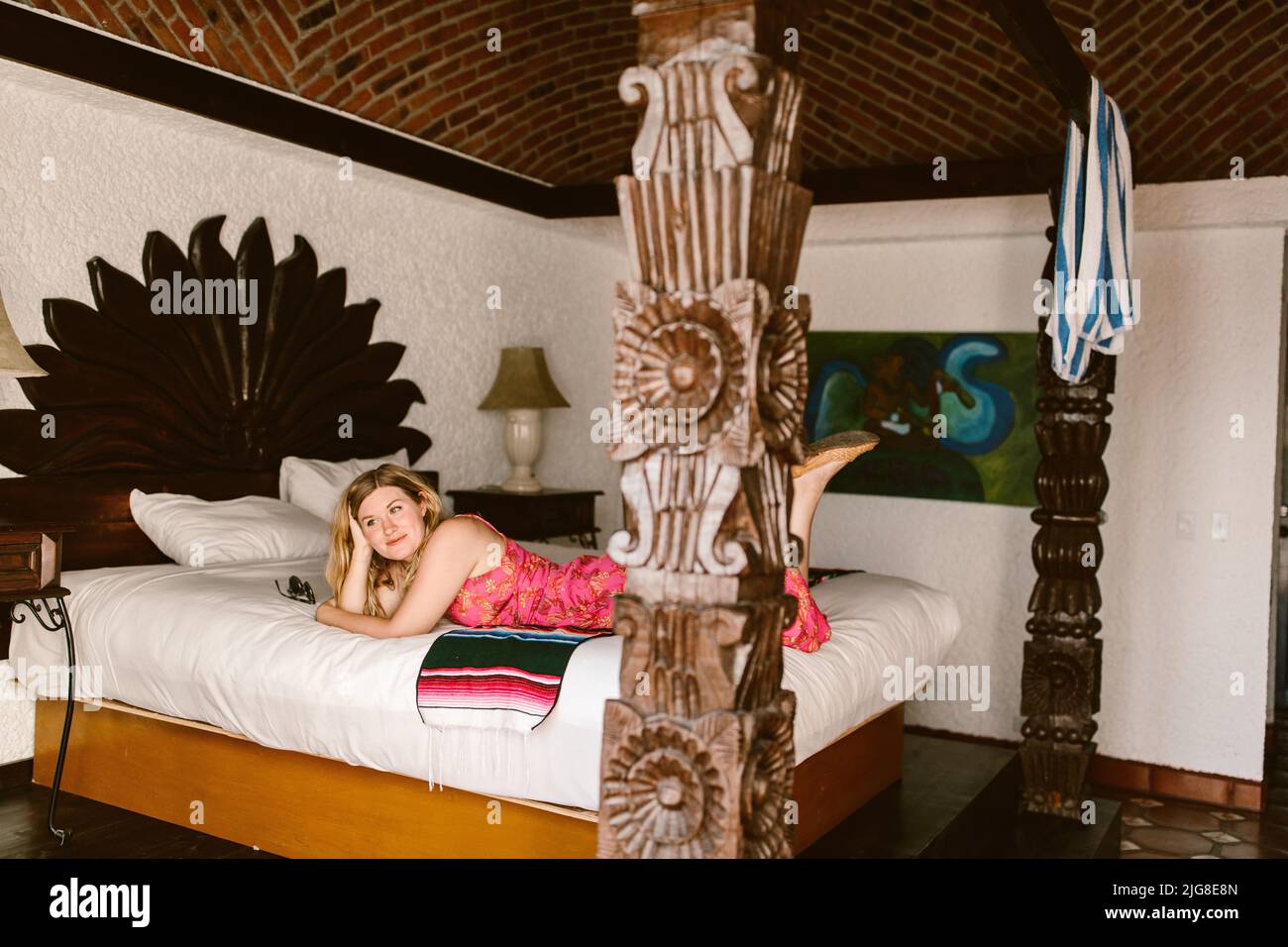 A Caucasian female in a cute pink dress lying in a bed in a hotel room