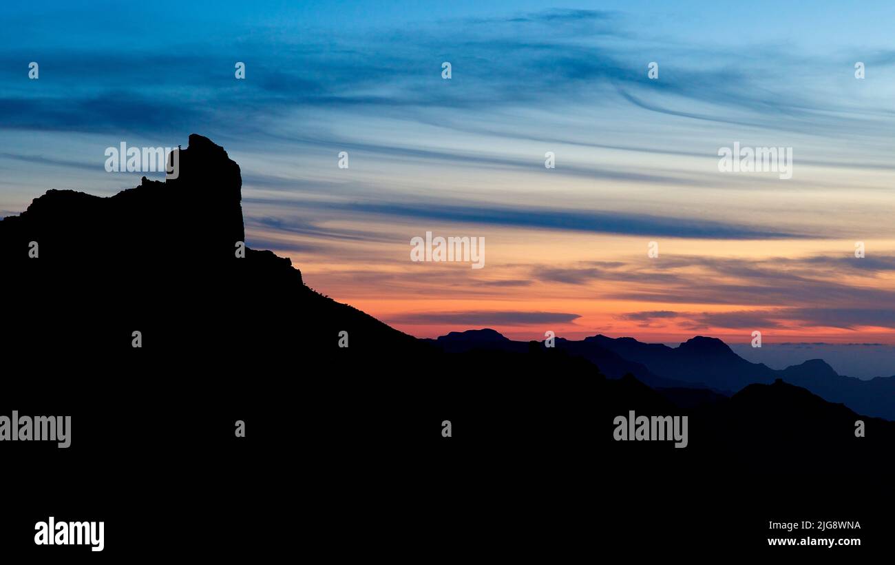 Spain, Canary Islands, Gran Canaria, Massif Central, Roque Bentayga, monolithic rock, close, silhouette, dusk, sky blue with dark blue clouds, orange sky stripe Stock Photo
