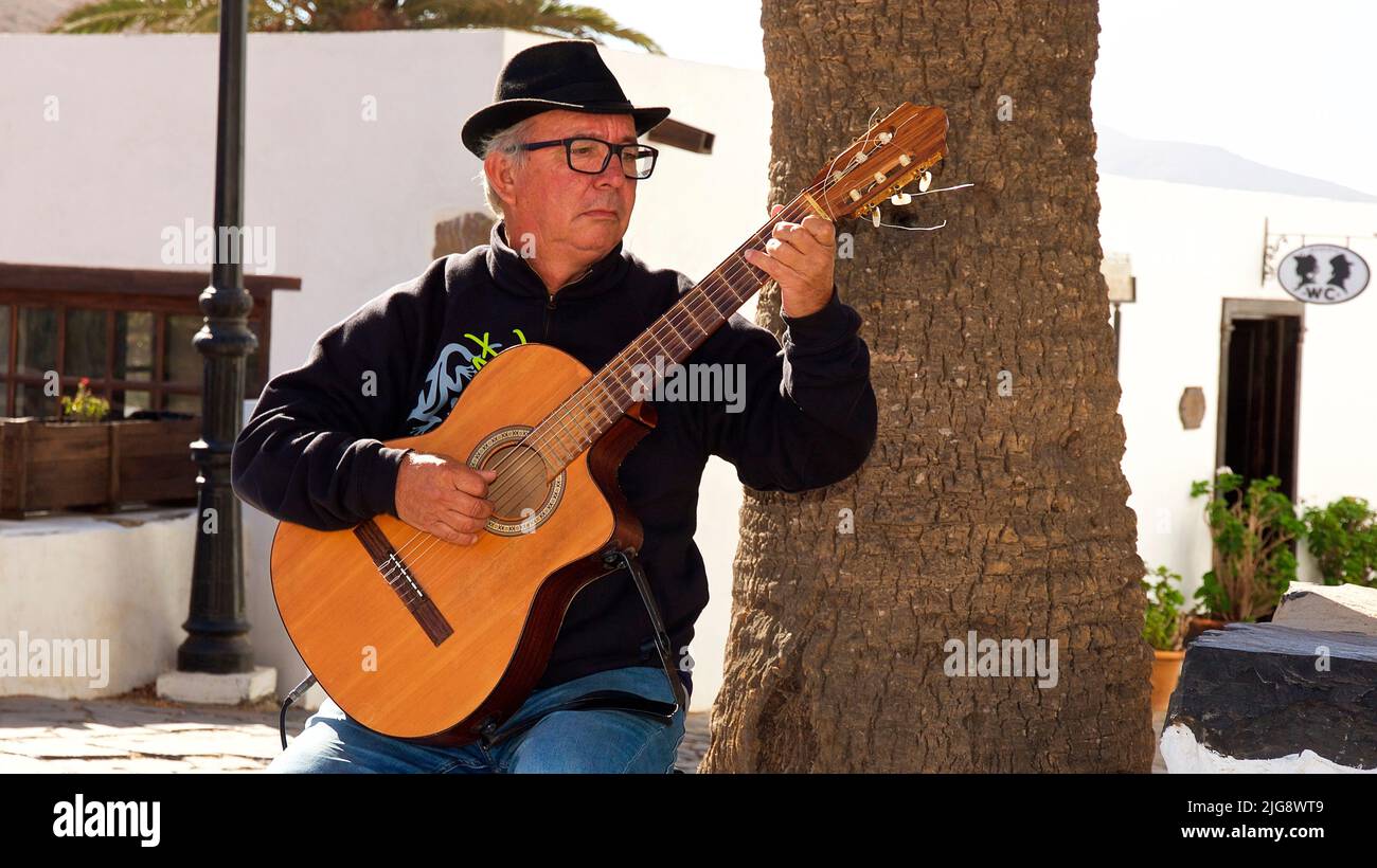 Spain, Canary Islands, Fuerteventura, Betancuria, old capital, old town, guitar player sitting in front of tree Stock Photo