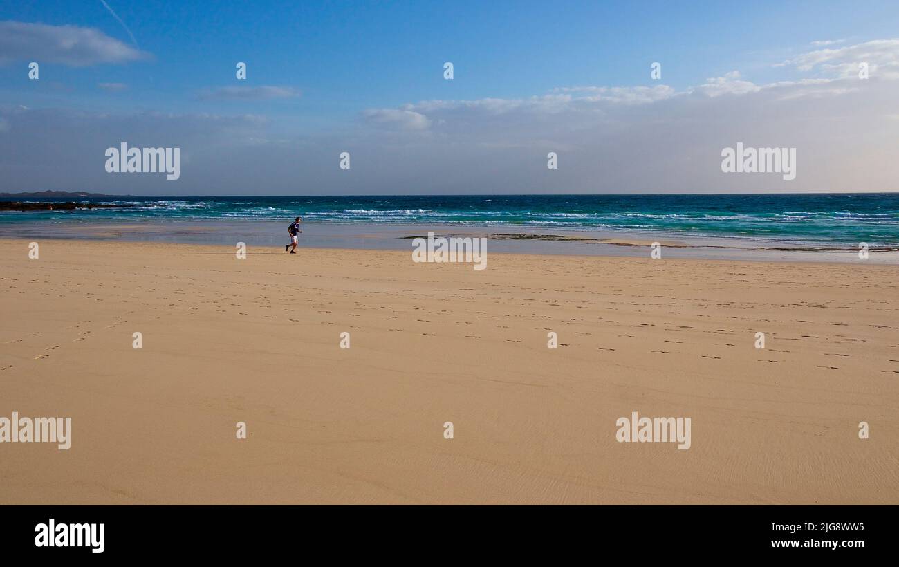Spain, Canary Islands, Fuerteventura, Corralejo, lonely jogger on sandy beach, sky blue, cloud bank white Stock Photo