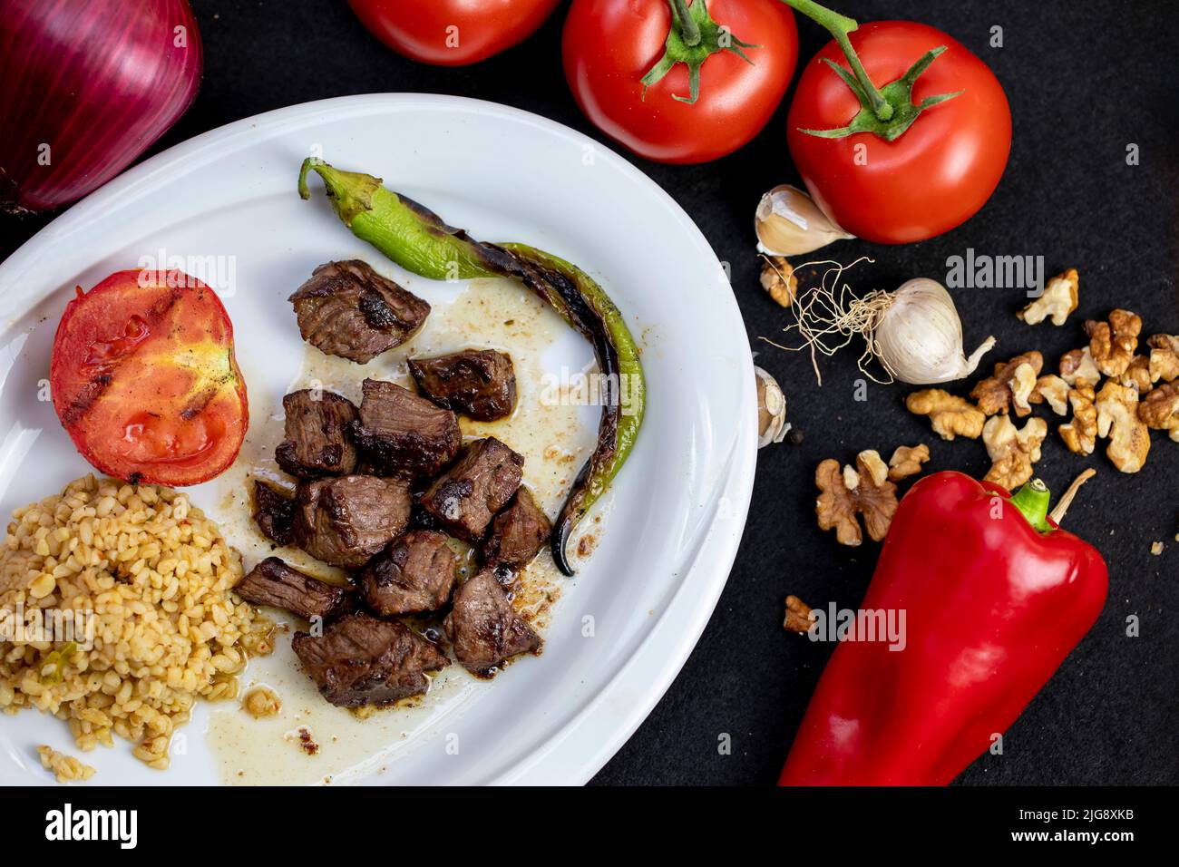 portions of cubed meat, served with tomatoes and roast vegetables on an plate Stock Photo