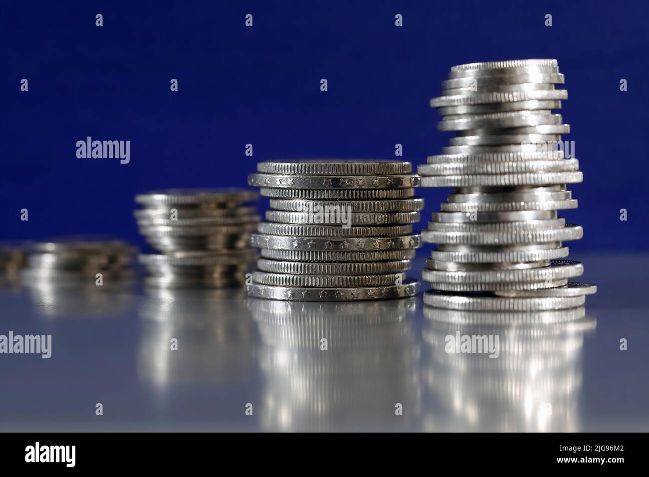 Here are four piles of coins which have been stacked on a grey, flat surface and on a dark blue background. Stock Photo