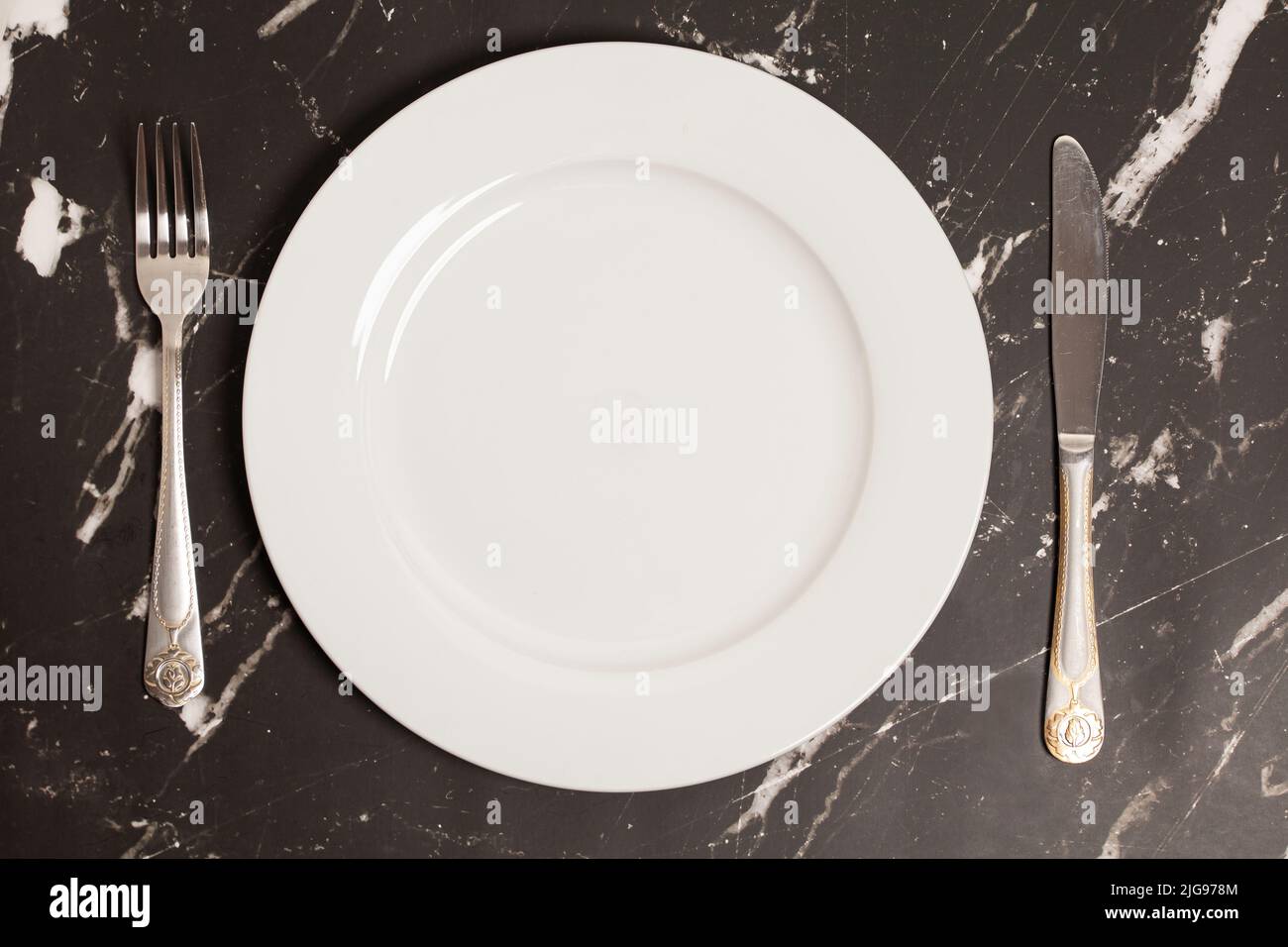 Knife and fork with plate on a marble background, top view Stock Photo