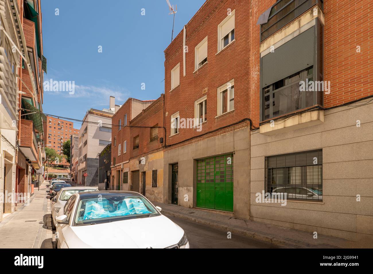 Facade of residential buildings in a narrow street full of parked cars and nice blue sky day Stock Photo