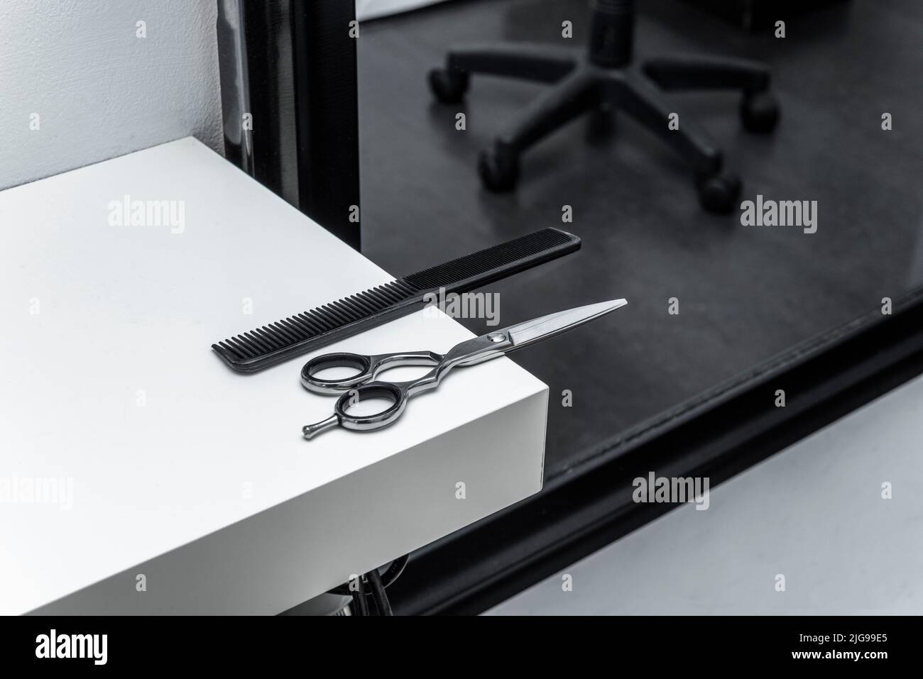 Stainless steel scissors and a black barber's comb on a wide white