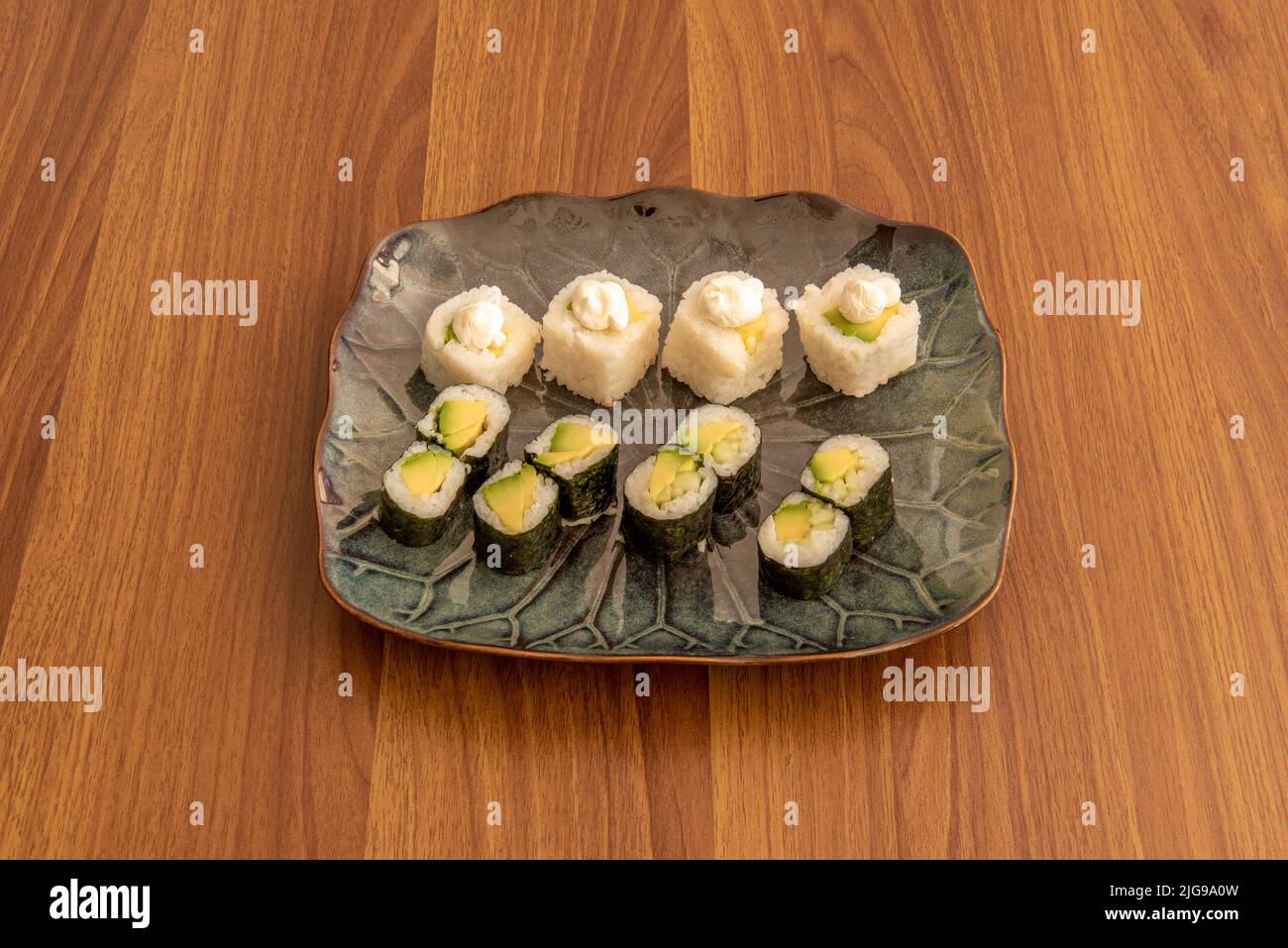 Porcelain tray with mixed avocado maki sushi and uramaki roll with sauce, white rice and nori seaweed Stock Photo