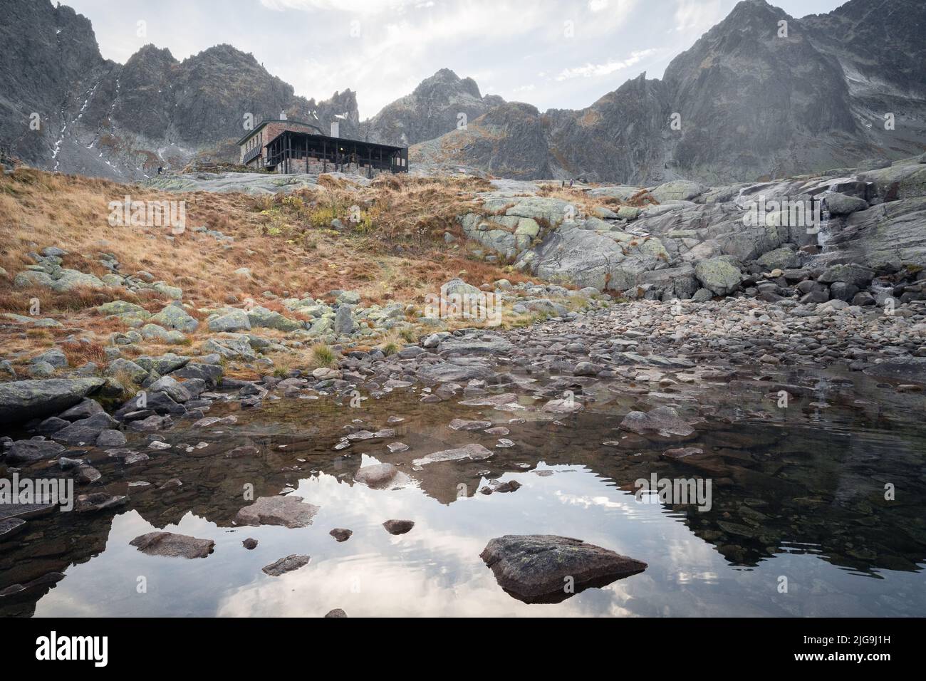 Stone mountain hut on the bank of alpine tarn surrounded by rocky peaks, Slovakia, Europe Stock Photo