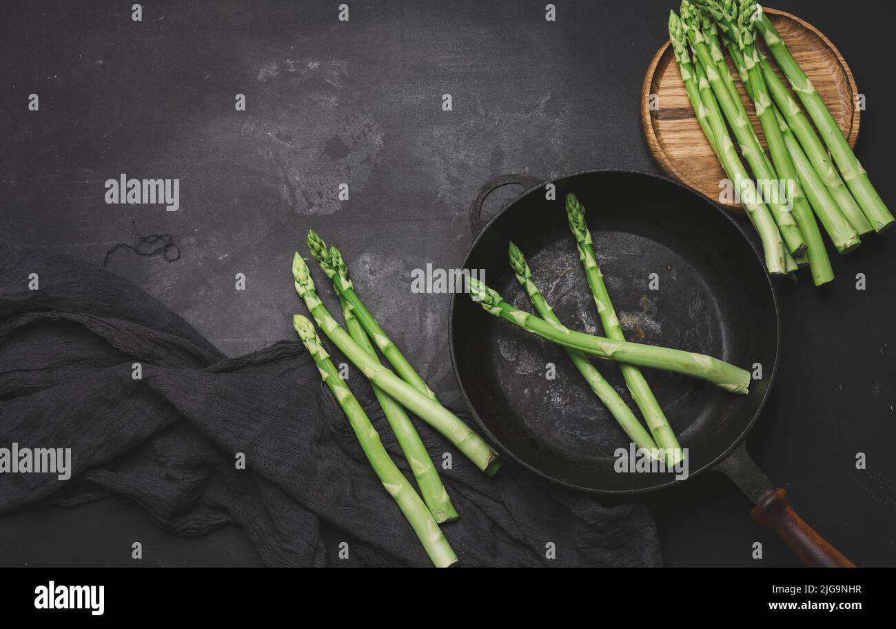 Fresh green asparagus in a round cast iron pan on a black table, top view Stock Photo