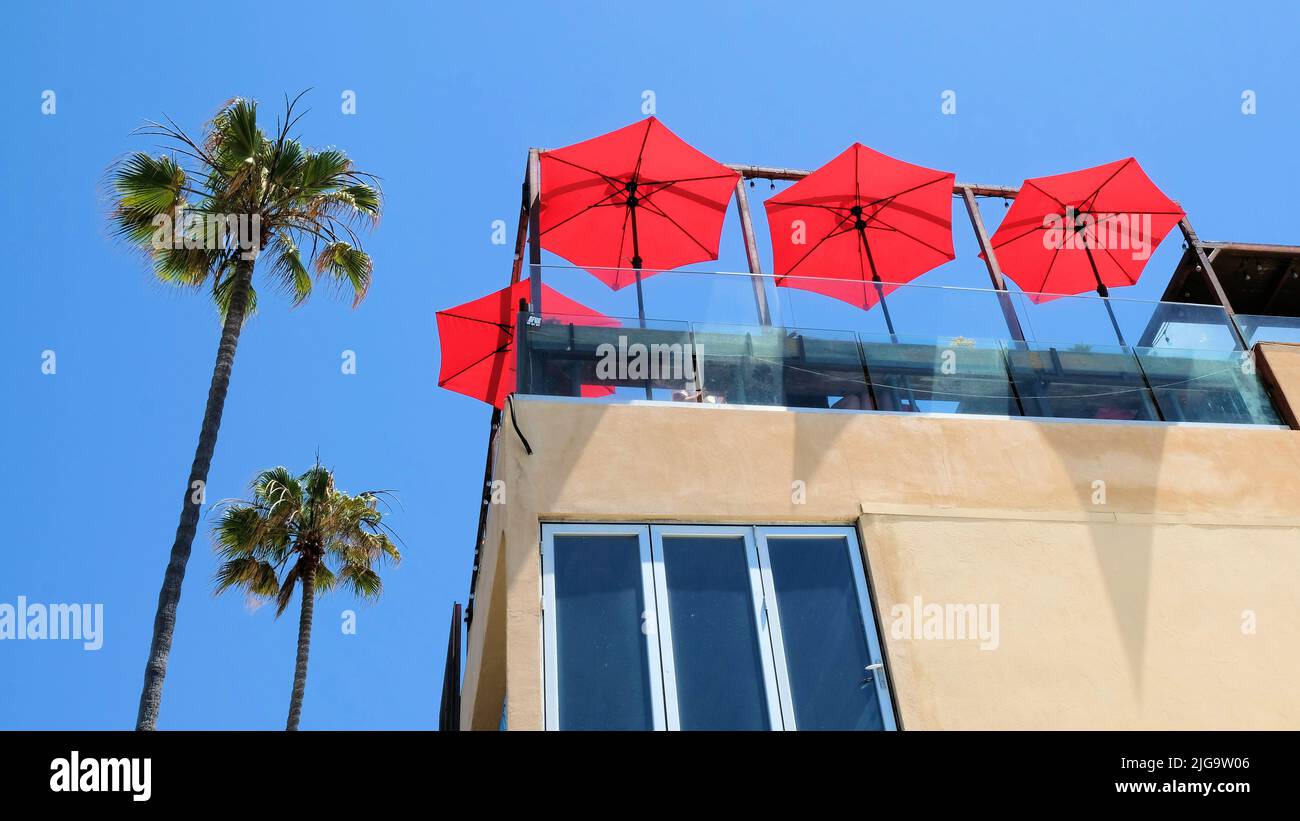 Exterior design concept for beach travel theme; red umbrellas, clear blue sky, palm trees at Ocean Beach, San Diego, California, USA; SoCal vibe. Stock Photo