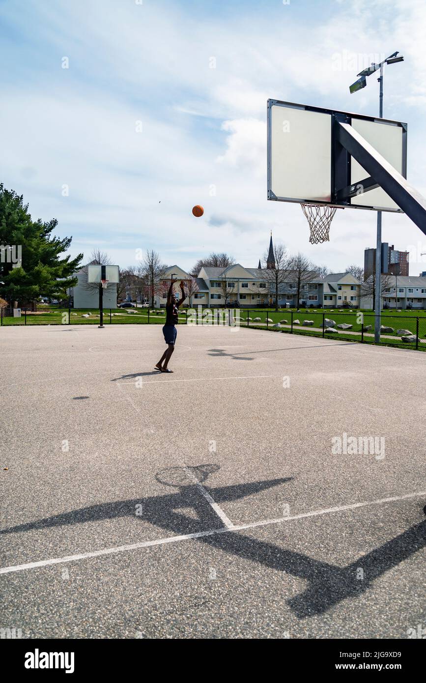 Portland, Maine -April 4, 2022: Cute teenager iplaying basketball. Young boy with red ball shooting on the city court. Hobby for kids, active lifestyl Stock Photo