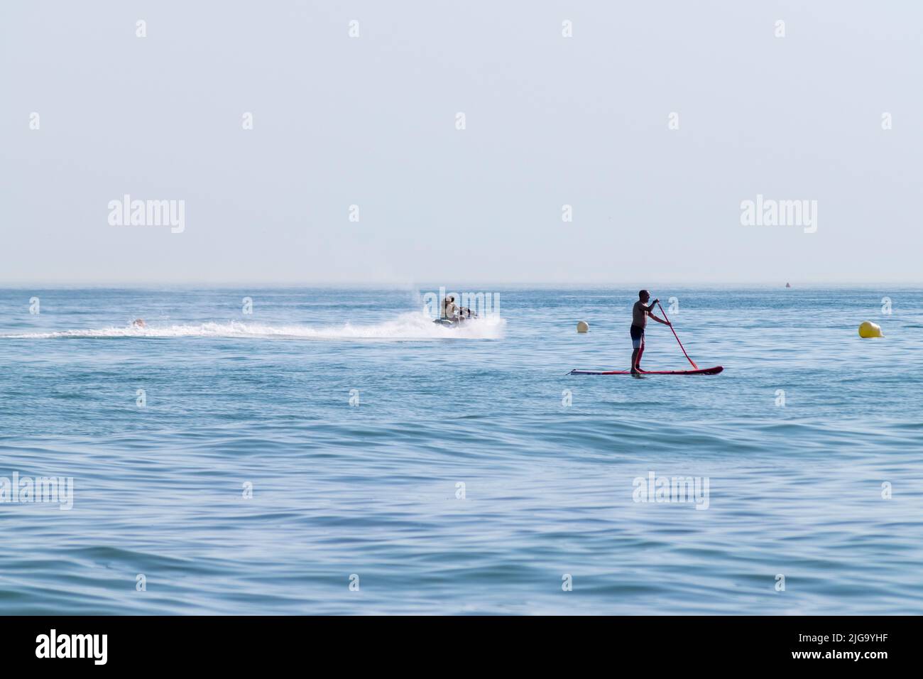 Ocean paddle, man standing on paddle board on the coast beach. Summer activities on vacations or hollydays. Beach business and hobbies. Secure area. Stock Photo