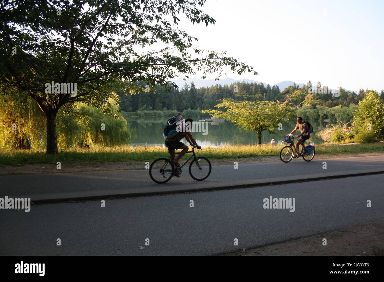 a shot of two bicyclists riding past Lost Lagoon Lake in Stanley Park, Vancouver, British Columbia, Canada Stock Photo