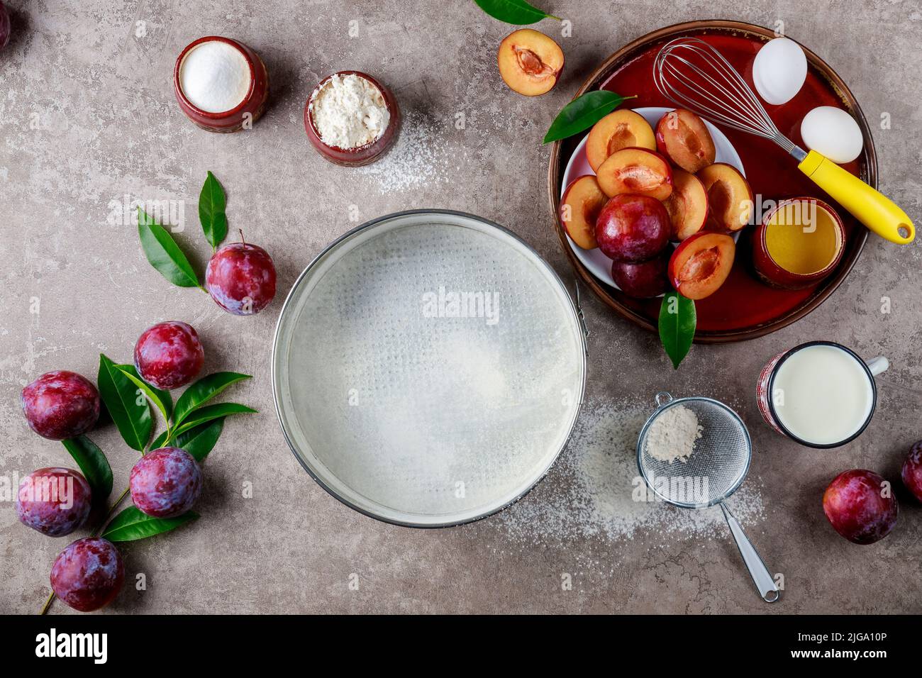 Using eggs, whisk, plum, and a baking pan are used in the baking process. Stock Photo