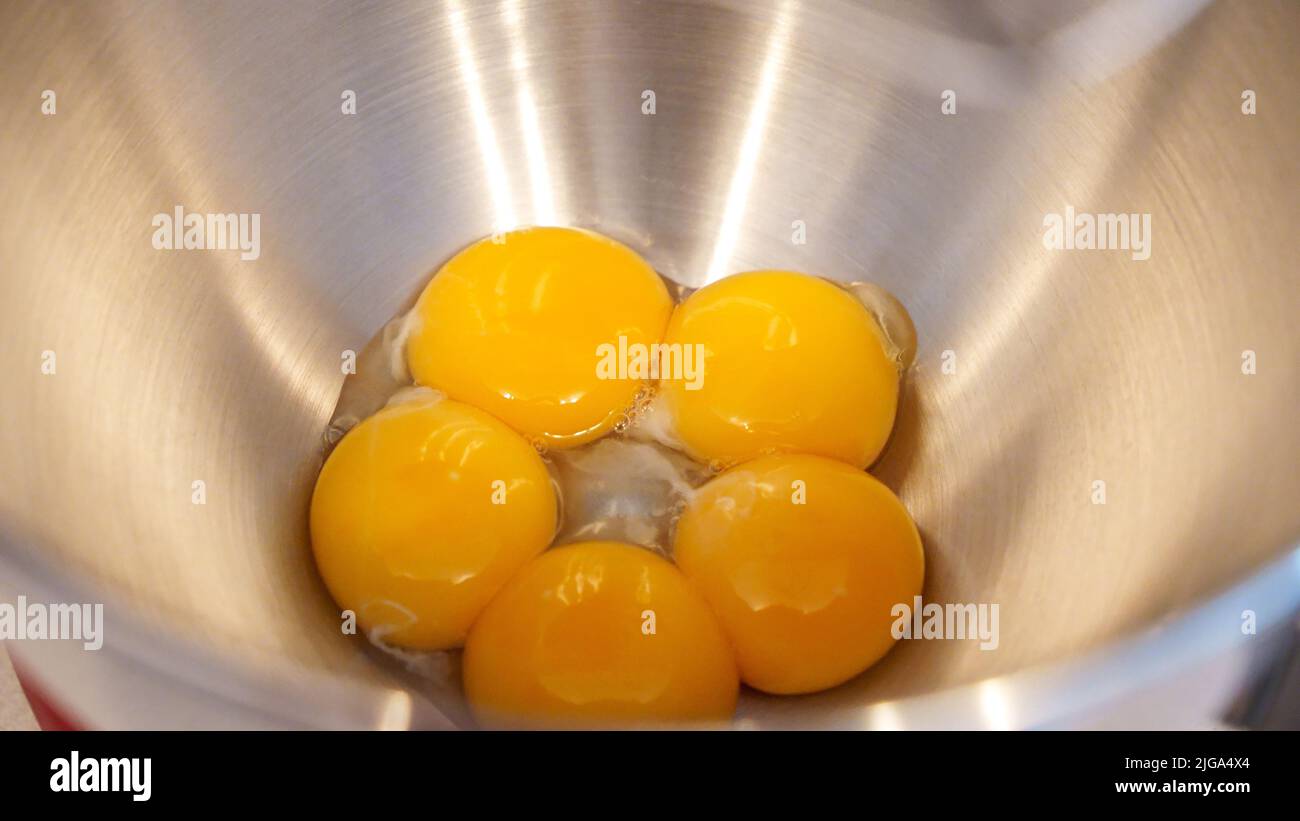 Raw eggs in a metal bowl of standing mixer. Preparing egg yolk with sugar in kitchen mixer Stock Photo